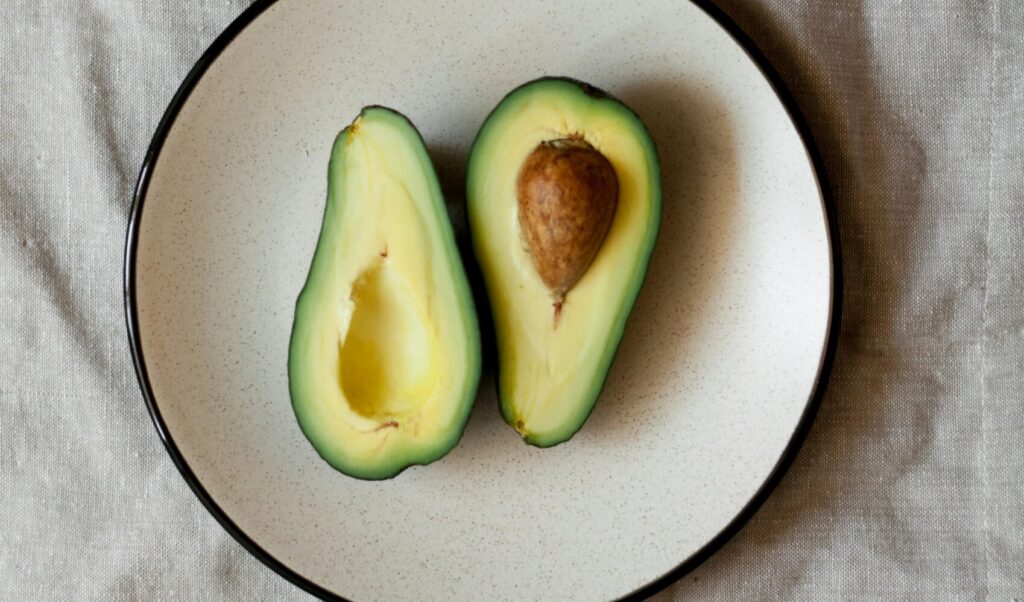 A variety of top plant-based anti-inflammatory foods, including avocado, chickpeas, green beans, peas, mushrooms, garlic, olives, fresh salad, and vegetable-based sauces, arranged around a wooden cutting board